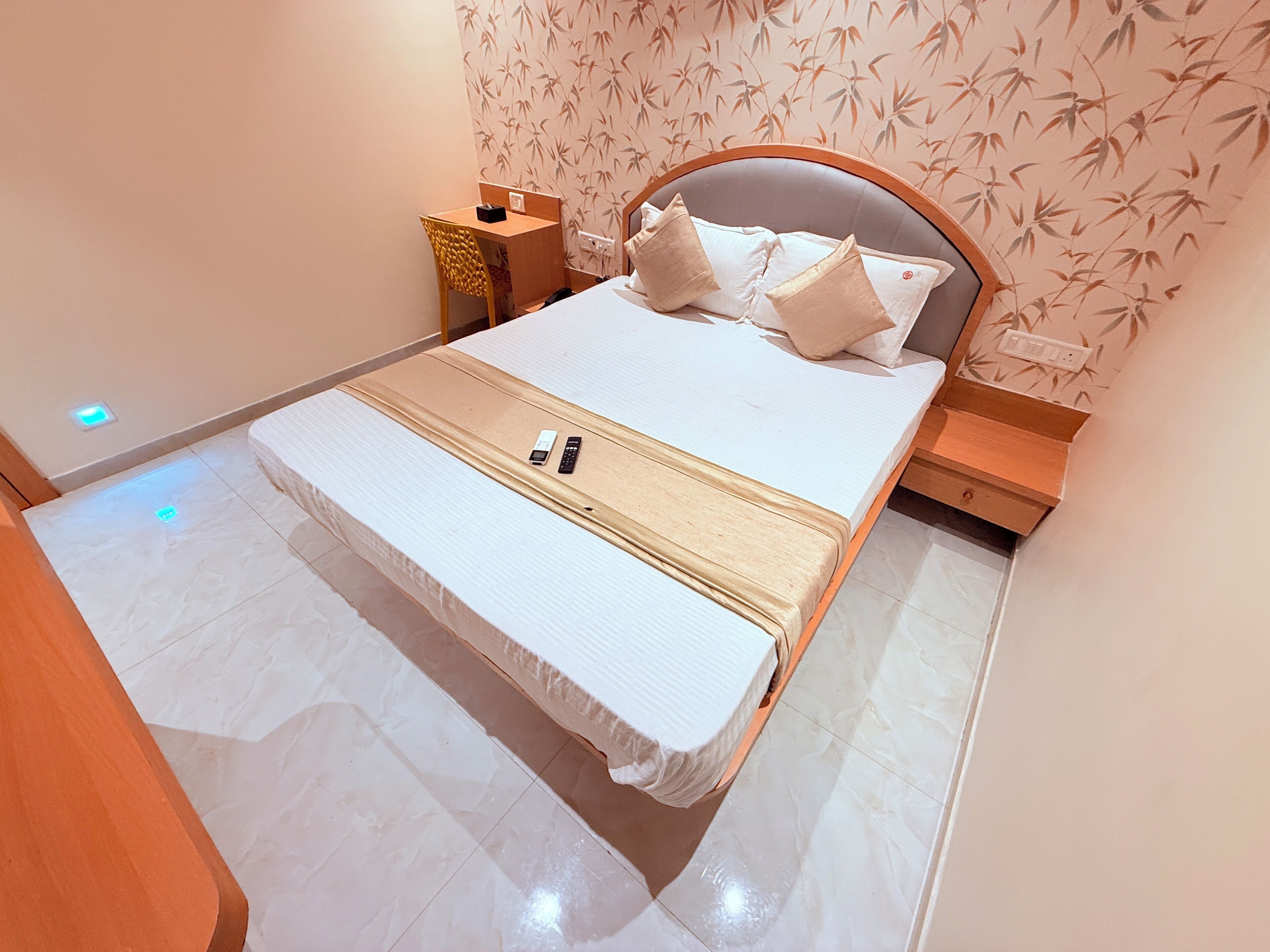 Cama bem arrumada com almofadas, mesa de cabeceira, cadeira e parede com padrão de bambu.