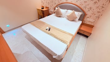 Cama bem arrumada com almofadas, mesa de cabeceira, cadeira e parede com padrão de bambu.