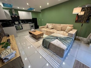 A modern living room with a sofa, coffee table, and a kitchen in the background. - Stylish 2 Bed Flat Parking Sutton Coldfield (Sutton Coldfield)