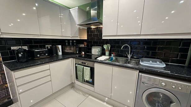 A modern kitchen with white cabinets, a black countertop, a built-in microwave, a coffee maker, and a washing machine.