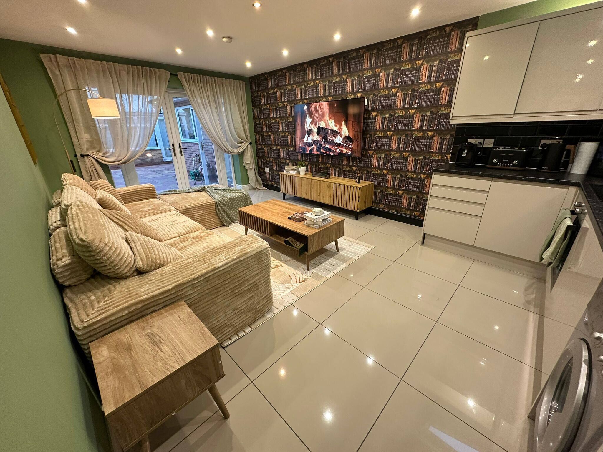 A modern living room with a sofa, coffee table, TV, bookshelf, and kitchen area.