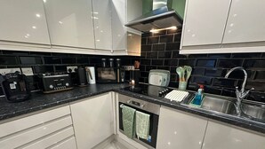 A modern kitchen with white cabinets, black tiled backsplash, stainless steel appliances, and a built-in dishwasher.