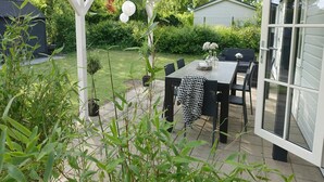 A covered patio with a table and chairs, surrounded by greenery and a house in the background. - Vechtdal Chalet de Berk (Rheezerveen)