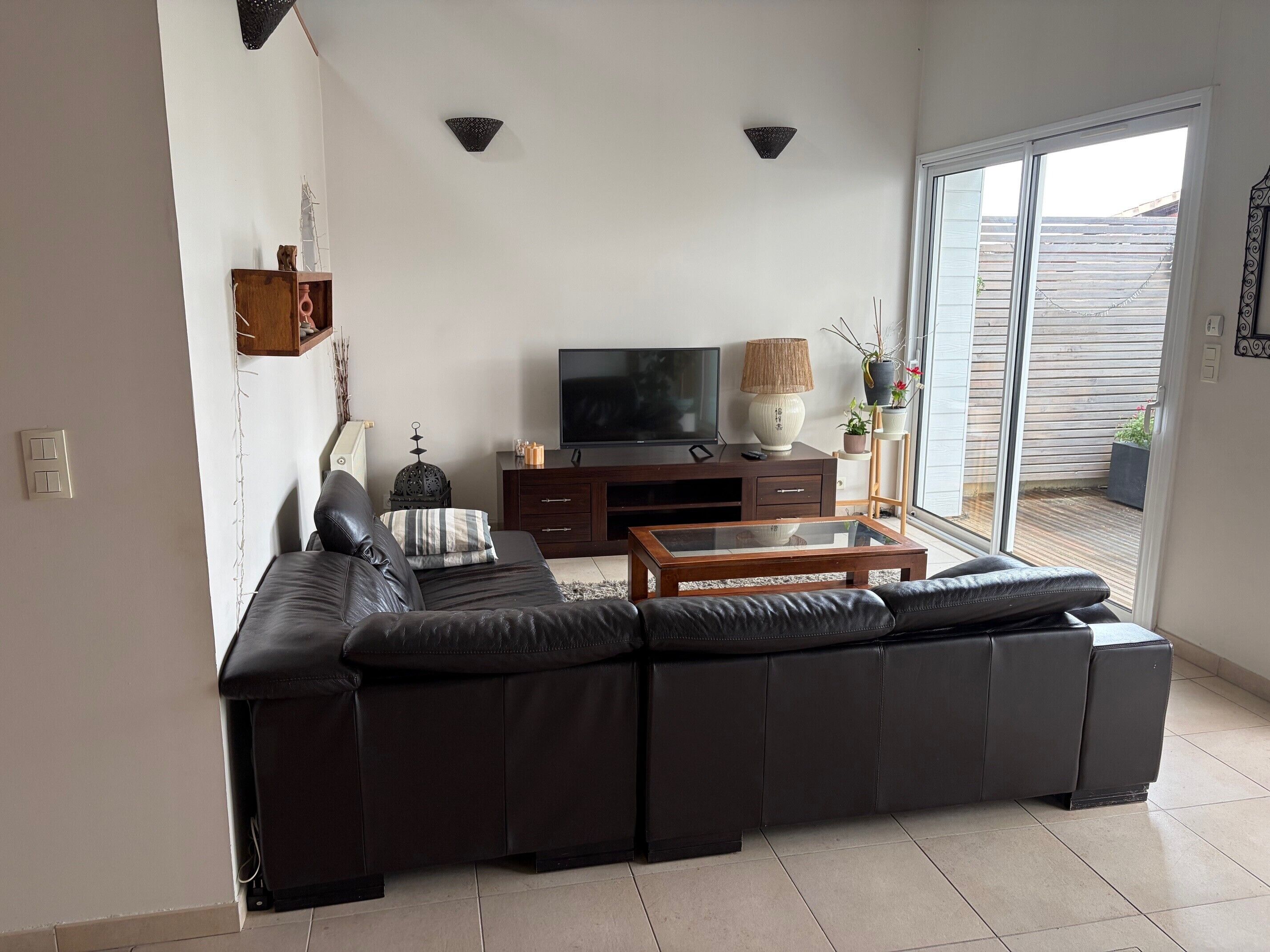 Un salon comprenant un canapé d’angle, un téléviseur, une table basse et une porte-fenêtre coulissante donnant sur un espace extérieur.