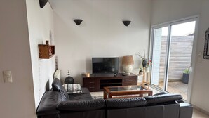 Ein Wohnzimmer mit einer Eckcouch, einem Fernseher, einem Couchtisch und einer Glasschiebetür zu einem Außenbereich.