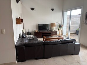 Ein Wohnzimmer mit einer Eckcouch, einem Fernseher, einem Couchtisch und einer Glasschiebetür zu einem Außenbereich.