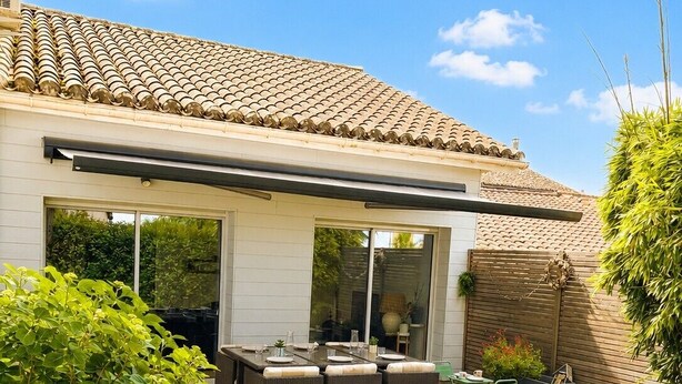 Ein Haus mit Terrasse, Sitzgelegenheit im Freien und einem überdachten Bereich.