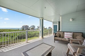 Eine überdachte Veranda mit Blick auf den Ozean, ein Korbsessel und ein Tisch.