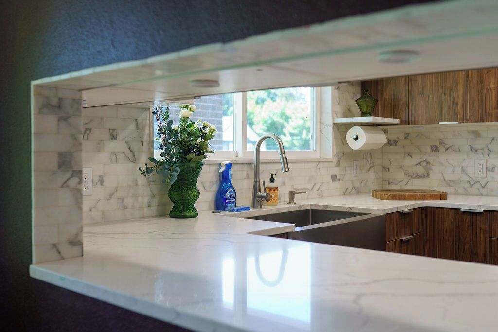 A kitchen with a marble backsplash, a window, a sink, and a green vase with flowers.