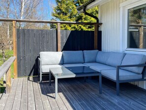 Eine Holzterrasse mit einem grauen Ecksofa und einem Glastisch.