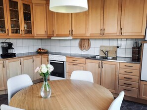A kitchen with wooden cabinets, a round dining table, a coffee maker, and a vase with flowers.