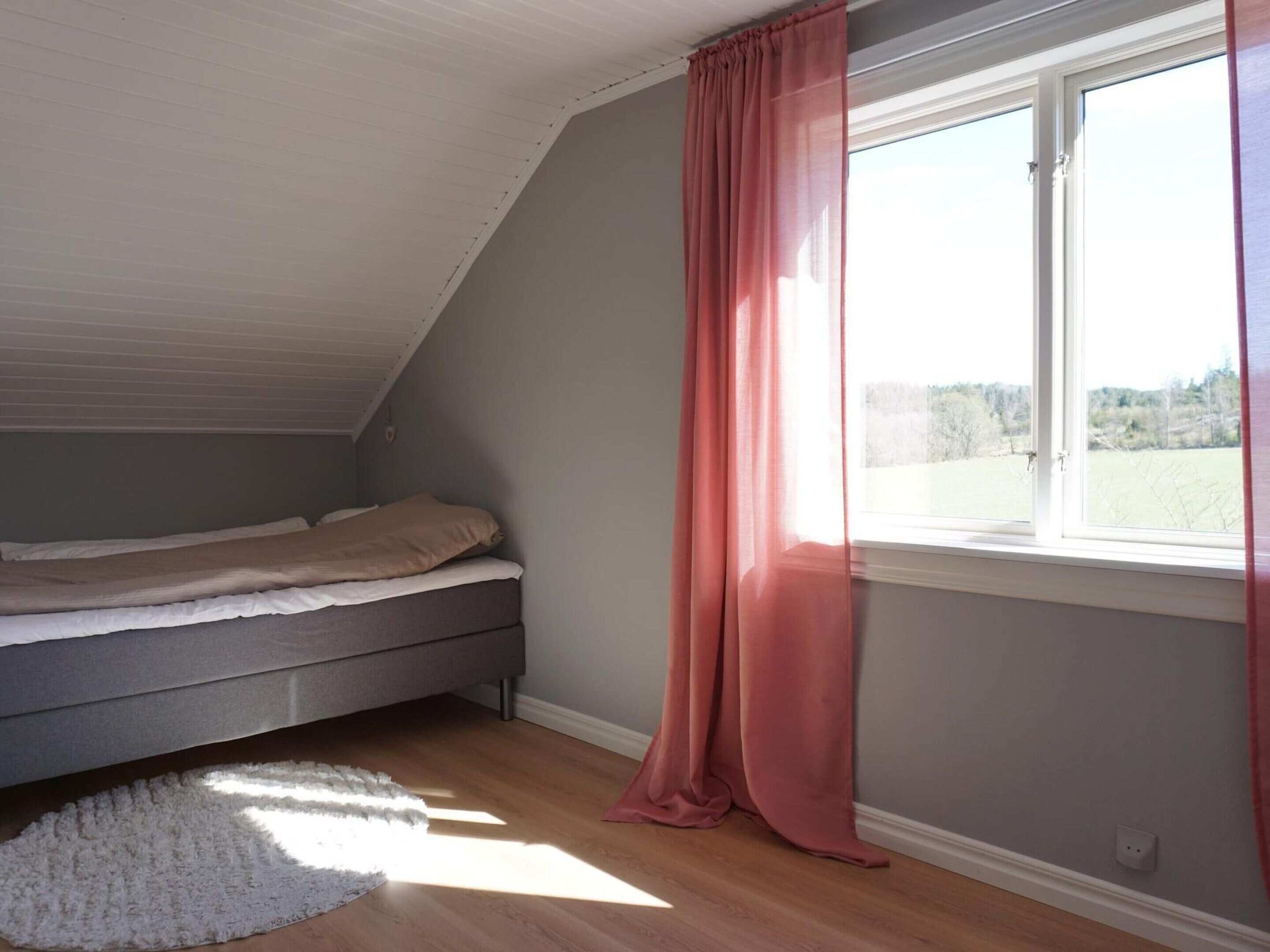 A bedroom with a single bed, a window with a view, and a white rug.