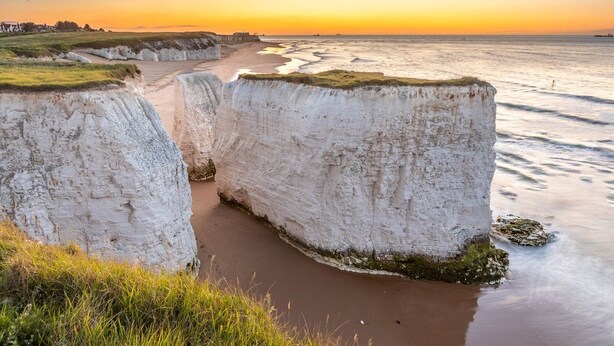 Eine Küstenlandschaft mit weißen Klippen, einem Sandstrand und Blick auf das Meer bei Sonnenuntergang.