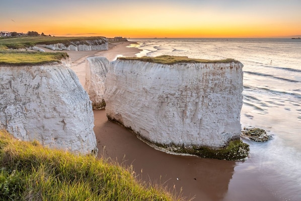 A coastal landscape with white cliffs, a sandy beach, and a view of the sea at sunset.