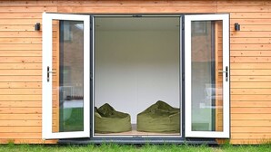Ein modernes Gebäude mit Holzfassade und einer Schiebetür. Im Inneren befinden sich zwei grüne Sitzsäcke.