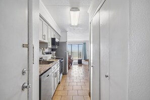 Ein schmaler Flur mit Küche, ausgestattet mit Schränken, einer Mikrowelle und einem Kühlschrank.