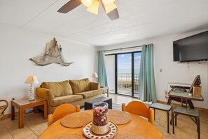 Ein Wohnzimmer mit einer Couch, einem Esstisch mit Stühlen, einem Fernseher und einem Balkon mit Blick.