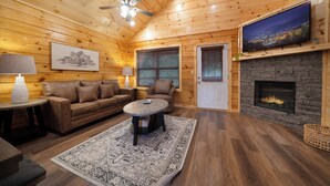 Ein gemütliches Blockhaus-Interieur mit Holzbalkendecke, Kamin, Fernseher und einer Couch.