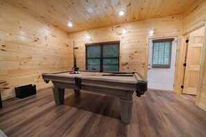 Uma mesa de bilhar em um quarto com paredes de madeira e uma porta.