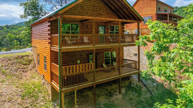 Eine zweistöckige Blockhütte mit Balkon und Terrasse, umgeben von viel Grün.