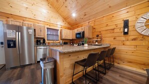 Eine Küche mit Holzwänden, einem Edelstahlkühlschrank, einer Mikrowelle, einem Spülbecken und einer Theke mit Stühlen.
