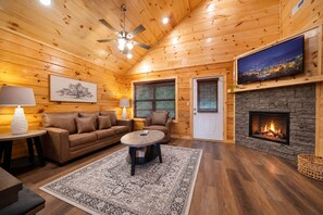 Ein gemütliches Blockhaus-Interieur mit Kamin, Holzwänden, Deckenventilator und Fernseher.