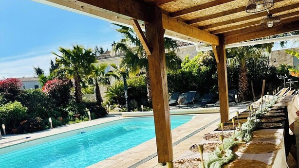 Ein Poolbereich mit einer Holzpergola, einem langen Tisch mit einer Zimmerpflanze und einem klaren, blauen Pool.