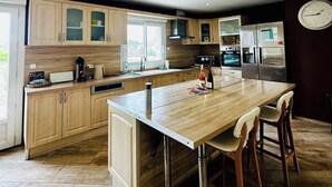 Eine moderne Küche mit Holzausstattung, einer zentralen Kochinsel, Edelstahlgeräten und einer Uhr an der Wand.