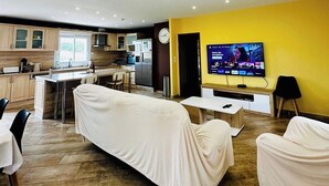 Ein modernes Wohnzimmer mit einer gepolsterten Couch, einem Essbereich, einer Küche und einem Fernseher, der einen Nachrichtensender zeigt.