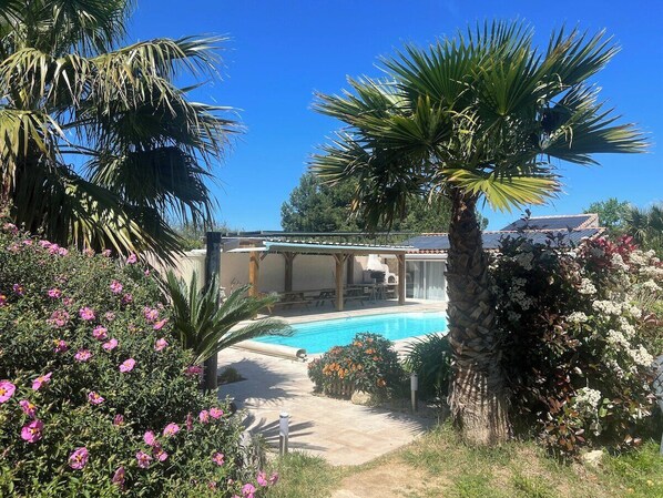 A swimming pool surrounded by lush greenery and a covered patio area.