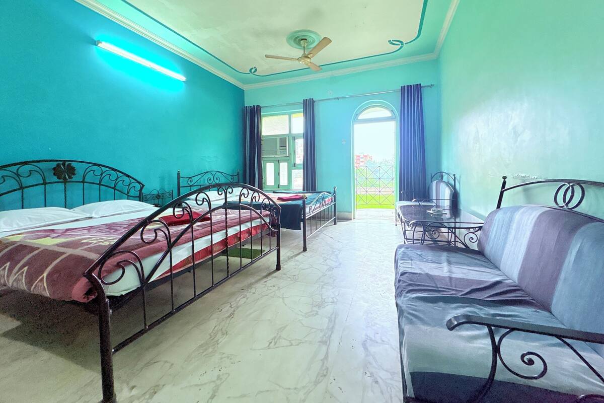A room with two beds, a sofa, a ceiling fan, and a window with curtains.