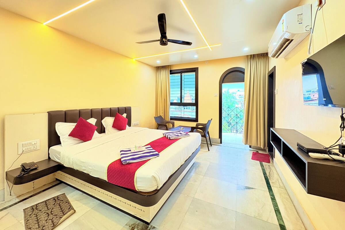 A hotel room with a bed, bedside table, air conditioning unit, and a desk with a chair.