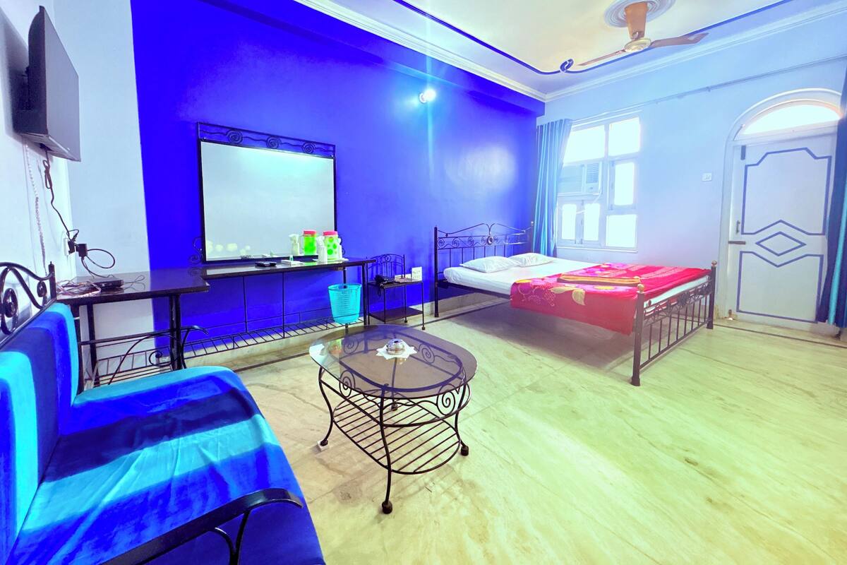 A room with a bed, a desk with a computer, a chair, a small table, and a television.