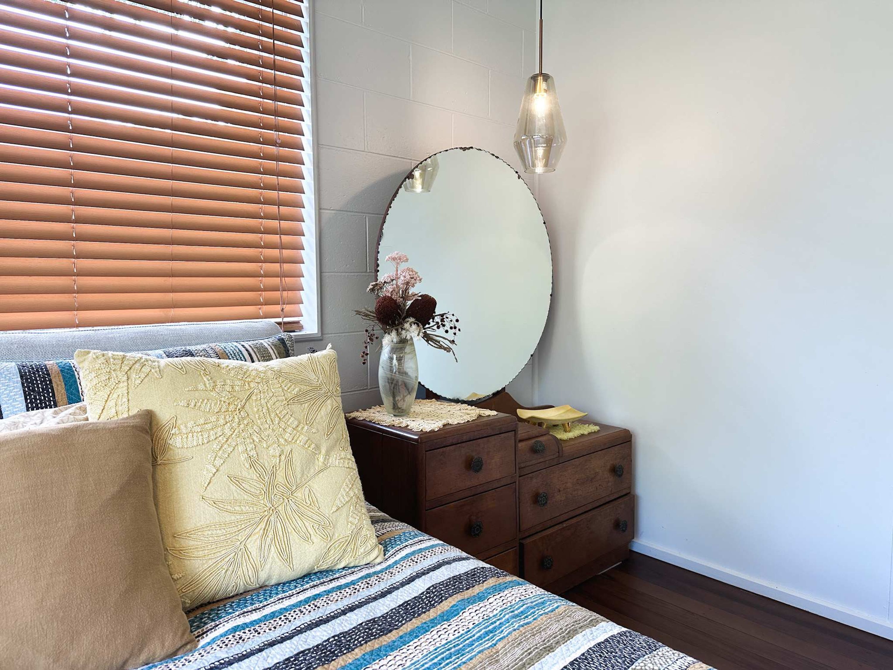 A bedroom with a bed, a dresser, a mirror, and a hanging light fixture.