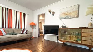 Una sala de estar con sofá, televisor y aparador con cristalería.