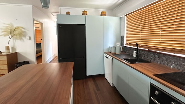 Una cocina moderna con encimera de madera, refrigerador negro, lavavajillas y ventana con persianas.