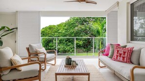 Uma varanda com vista para vegetação exuberante, um ventilador de teto e um sofá com almofadas.