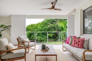 Uma varanda com vista para vegetação exuberante, um ventilador de teto e um sofá com almofadas.