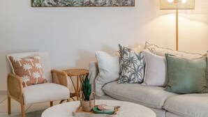 Uma sala de estar com uma mesa de centro redonda, um sofá, uma poltrona e uma pequena mesa com uma planta.