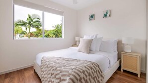 Quarto com cama, janela com vista para palmeiras, ventilador de teto e duas luminárias de cabeceira.
