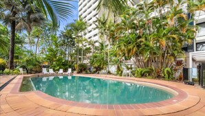 Una piscina con bordo piastrellato, circondata da palme e un edificio a più piani.