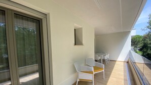 Uma varanda com porta de correr em vidro, uma mesa pequena e duas cadeiras brancas.