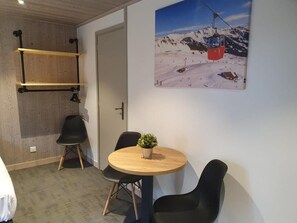 Una habitación con techo de madera, una mesa redonda de madera con sillas, una planta en maceta y una fotografía de un telesilla en la pared.