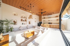 A modern living space with a wooden ceiling, built-in shelves, a kitchen area, and a seating area with a coffee table. - Disenta Villa by Tasvan (Badung)