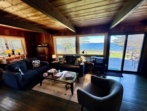 Interior acogedor de una cabaña con paredes de madera, un sofá, una mesa de centro y vistas al océano a través de amplias ventanas.