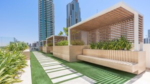A rooftop terrace with artificial grass, seating areas, planters with greenery, and modern buildings in the background. - Free Housekeeping Visits During Your Stay - Stayshort - Studio in Jumeirah Village Circle for 2 With Balcony (Dubai)
