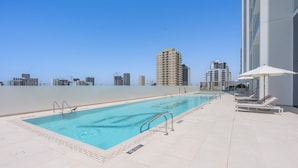A rooftop pool with a city view, lounge chairs, and a clear sky. - Free Housekeeping Visits During Your Stay - Stayshort - Studio in Jumeirah Village Circle for 2 With Balcony (Dubai)