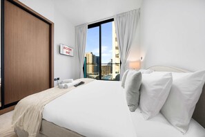 A hotel room with a large bed, a view of buildings, a sign reading 'BOOK ME,' and a wooden door. - Free Housekeeping Visits During Your Stay - Stayshort - Studio in Jumeirah Village Circle for 2 With Balcony (Dubai)