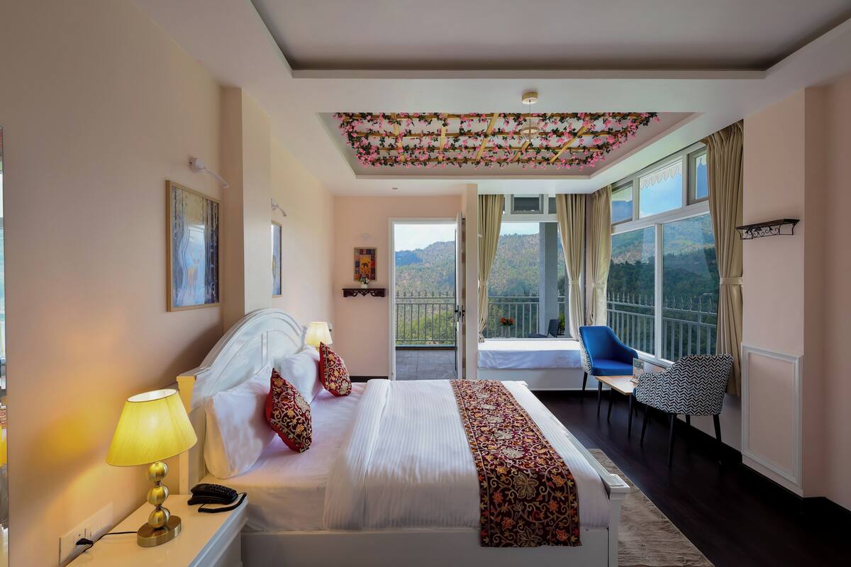 A hotel room with a bed, bedside lamp, a view of the outdoors, a window with curtains, and a balcony.