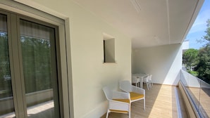 A balcony with a sliding glass door, a small table, and two white chairs. - Bright Accommodation 300m From the sea (San Michele al Tagliamento)